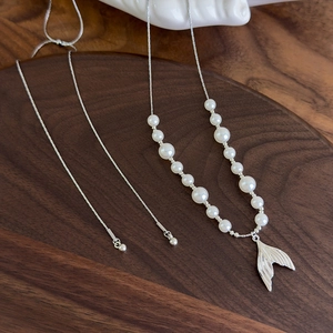 Close-up of pearl necklace featuring fishtail pendant and delicate silver chain on wood