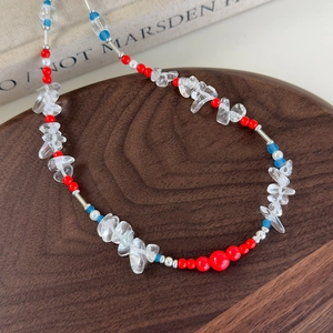 Detail of beaded necklace with red, blue beads and irregular clear stones on wood