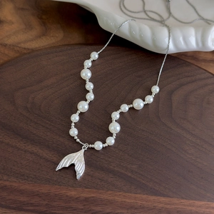Close-up of pearl necklace with a silver fishtail pendant on a minimalist ceramic plate