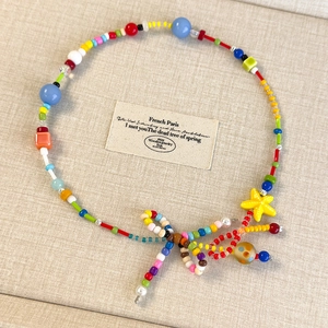 Dettaglio collana di perline colorate con ciondolo a stella gialla e fiocco intrecciato