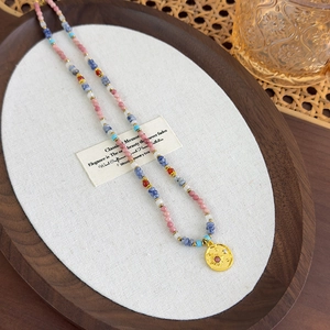 Pink stone beaded necklace with a golden sun pendant displayed on a premium velvet tray