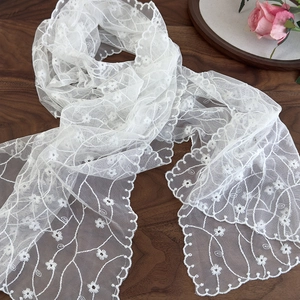 Detail of white mesh lace scarf with floral embroidery and scalloped edges on wood