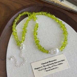 Detail of green peridot stone necklace featuring a white baroque pearl and silver clasp