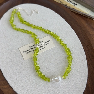 Macro detail of olive green stone necklace with a baroque pearl on linen texture
