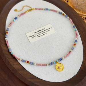 Close-up of a colorful beaded necklace with a sun pendant and pink stone heart tag