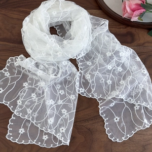 Detailed close-up of white floral embroidery on a soft mesh lace scarf with scalloped edges