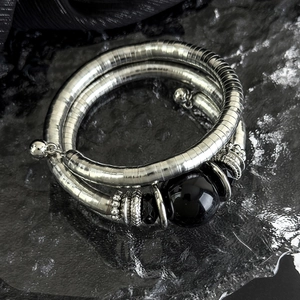 Detail of a triple-layer silver metal bracelet with black beads on a stone base