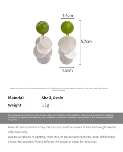 Détail des boucles d'oreilles en résine verte avec des pendentifs en coquillage blanc