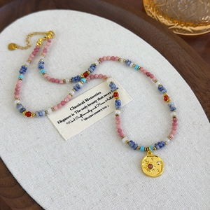Detail of beaded necklace with pink stones and golden sun pendant featuring a red center