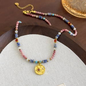Detail view of pink beaded necklace with gold sun pendant on a wooden jewelry tray