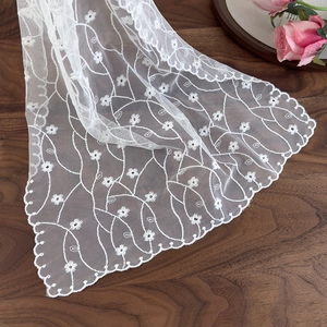 White daisy embroidery lace scarf on wood background with elegant scalloped edge