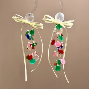 Close-up of dangling earrings featuring colorful sequins and a yellow ribbon bow