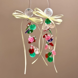 Macro detail of colorful shell discs and a yellow satin bow on these stylish drop earrings