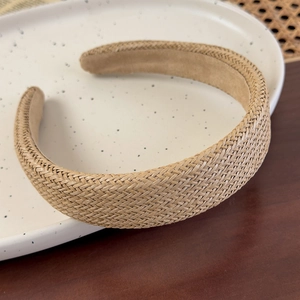 Close-up detail of a wide woven straw headband with soft velvet lining on a ceramic plate
