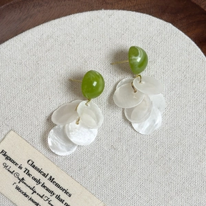 Vue détaillée de boucles d'oreilles en nacre verte et blanche sur plateau en bois
