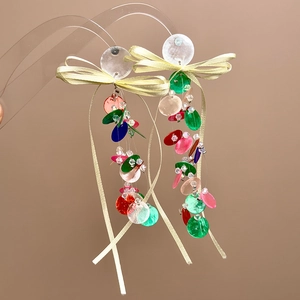 Close-up of colorful sequin fringe earrings with light yellow ribbon bow on acrylic stand