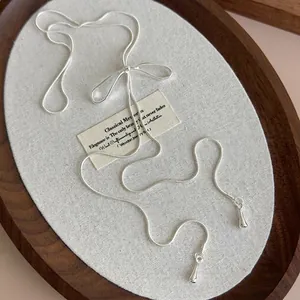 Collier nœud argenté avec pendentifs gouttes lisses sur un plateau en bois
