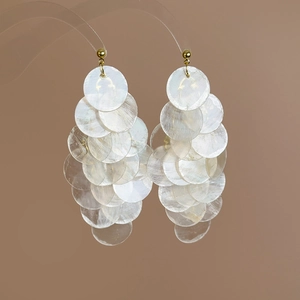 Detailed macro view of layered white pearlescent shell discs with golden bead ear hooks