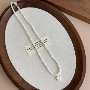 Elegant pearl necklace with brushed shell flower pendant on a walnut jewelry tray