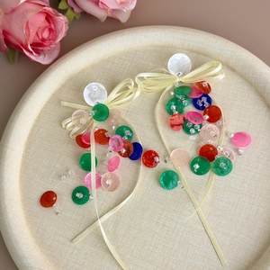 Detail of colorful disc bow earrings on a beige tray with soft floral accents