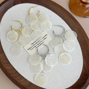 Detail of gold and silver hoop earrings with layered seashell discs on a wooden tray