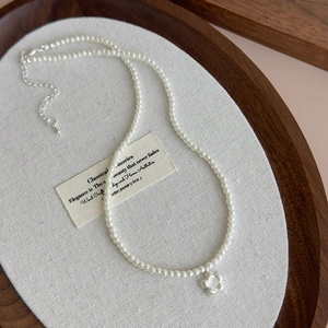 Close-up of pearl necklace featuring a mother-of-pearl flower pendant on gray fabric