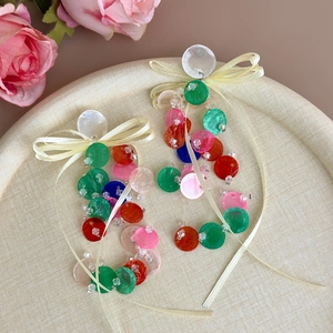 Close-up of long fringe earrings with colorful sequins, shell detail and ribbon bow