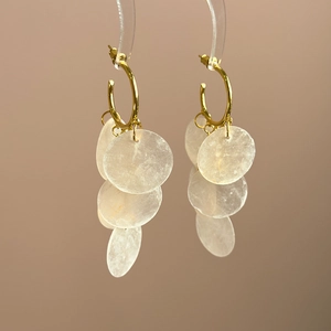 Detailed view of long shell tassel earrings with gold rings on a display stand
