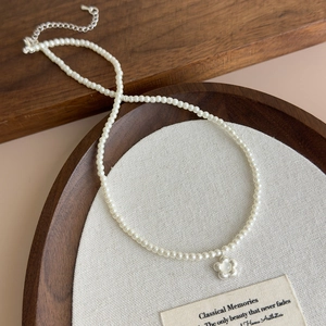 Macro shot of a pearl necklace with a brushed flower pendant and silver metal lobster clasp