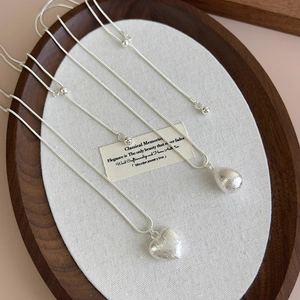 Detail of silver heart and waterdrop pendants with brushed texture on snake chain