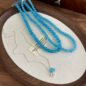 Detailed close-up of blue cat eye stone flower pendant with layered silver necklace set