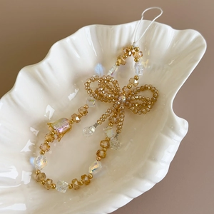 Detail of beaded phone strap with amber crystals and a delicate bow in a shell dish