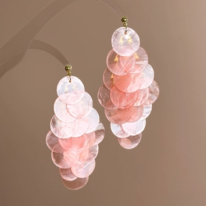 Detailed close-up of pink iridescent shell fringe earrings on a luxury display stand