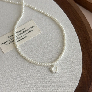 Close-up of pearl necklace with a brushed metal flower pendant and opal stone center