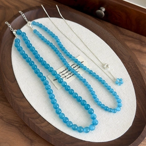 Detail of blue cat eye stone bead necklace with a silver flower pendant in a wooden tray
