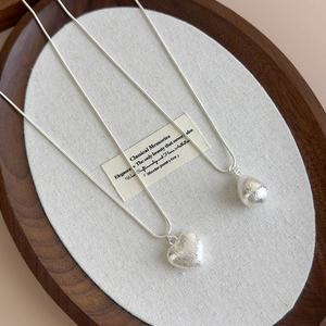 Detail of silver heart and water drop necklaces with brushed texture on wooden tray