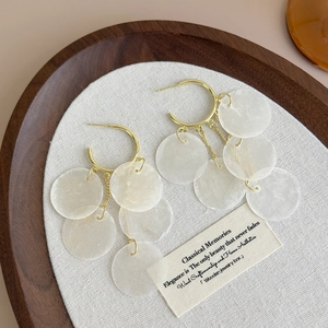 Golden C-shaped hoop earrings with dangling shell discs for a summer beach vacation style