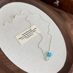 Close-up of blue cat-eye stone flower pendant on silver chain over linen texture