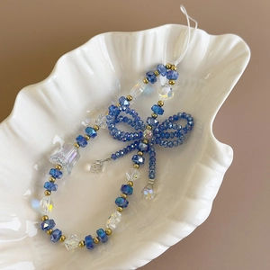 Close-up of blue crystal beaded phone charm with bowknot on shell ceramic tray