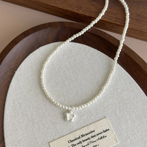 Detail of elegant pearl necklace featuring a silver flower pendant on a rustic wood tray