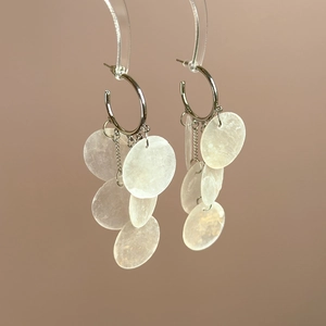 Detail view of silver hoop earrings featuring hanging translucent shell pendants on a stand