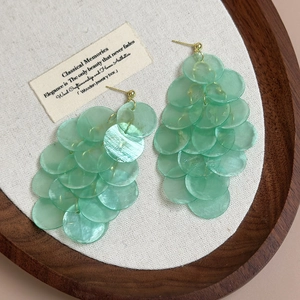 Detail of mint green shell earrings with gold metal studs on linen background