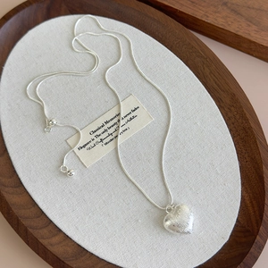 Detail of silver heart necklace with brushed metal texture and sleek snake chain link