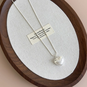 Close-up of heart-shaped pendant with brushed silver texture and elegant snake chain