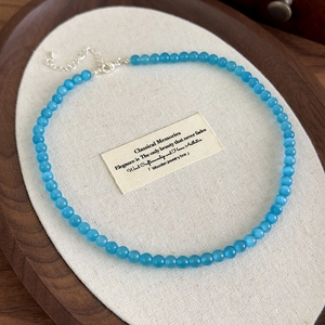 Detail of blue cat eye stone bead necklace with silver lobster clasp on a wooden tray