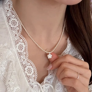 Elegant pearl necklace with a brushed shell flower pendant worn on a collarbone