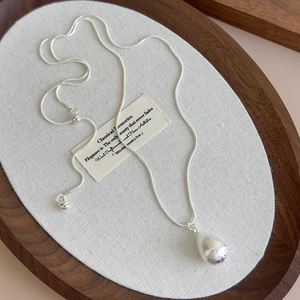 Macro detail of silver teardrop pendant with brushed texture on adjustable snake chain