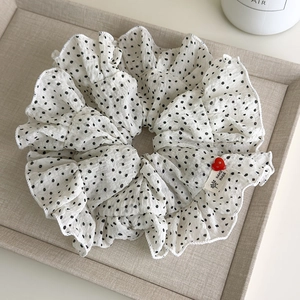 Close-up of white polka dot scrunchie with ruffled edges and red heart button detail