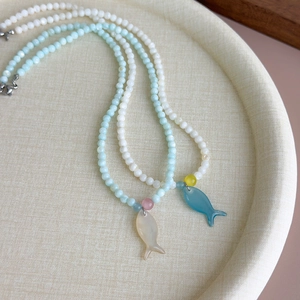 Détail de colliers en perles avec pendentifs poissons bleu et menthe sur plateau