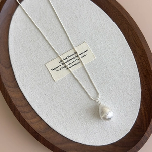 Macro detail of brushed silver teardrop pendant and elegant snake chain on white fabric